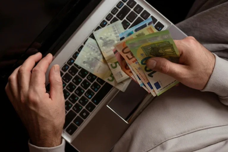 Person holding banknotes over a laptop